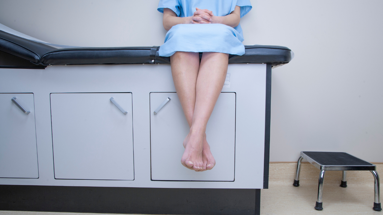 female patient at doctor's office waiting on an examination table in gown
